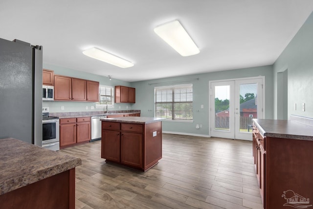 kitchen featuring french doors, a kitchen island, appliances with stainless steel finishes, wood-type flooring, and sink