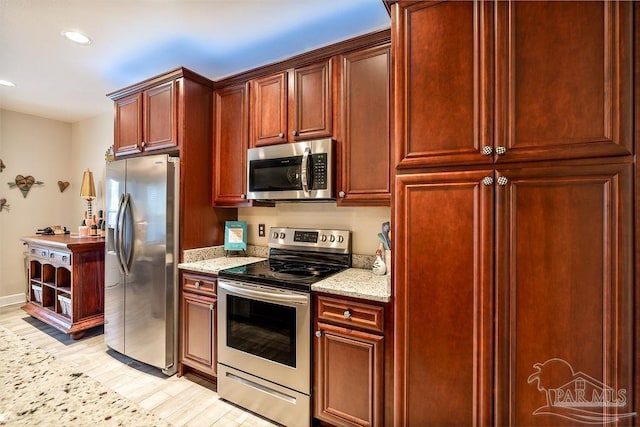 kitchen with light wood finished floors, stainless steel appliances, light stone counters, and reddish brown cabinets