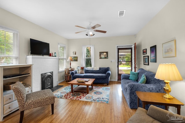 living room featuring a brick fireplace, light hardwood / wood-style floors, and ceiling fan