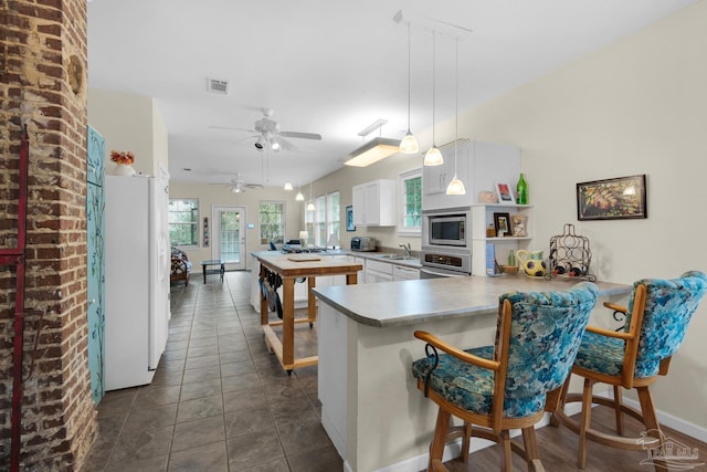 kitchen featuring a breakfast bar, white cabinets, kitchen peninsula, hanging light fixtures, and stainless steel appliances