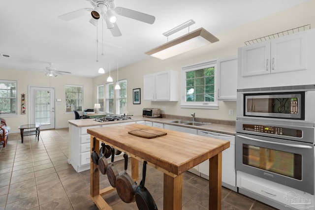 kitchen with appliances with stainless steel finishes, hanging light fixtures, white cabinets, ceiling fan, and sink