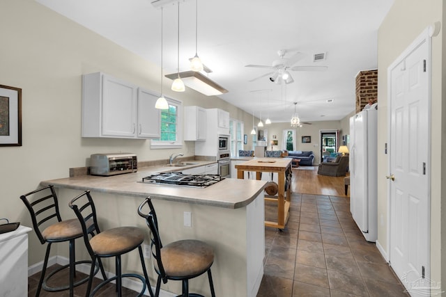 kitchen featuring kitchen peninsula, white cabinetry, pendant lighting, and stainless steel appliances