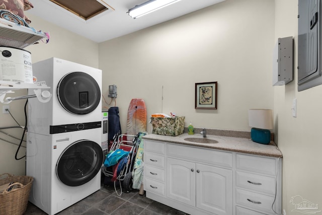 washroom featuring dark tile patterned flooring, stacked washer / dryer, cabinets, and sink