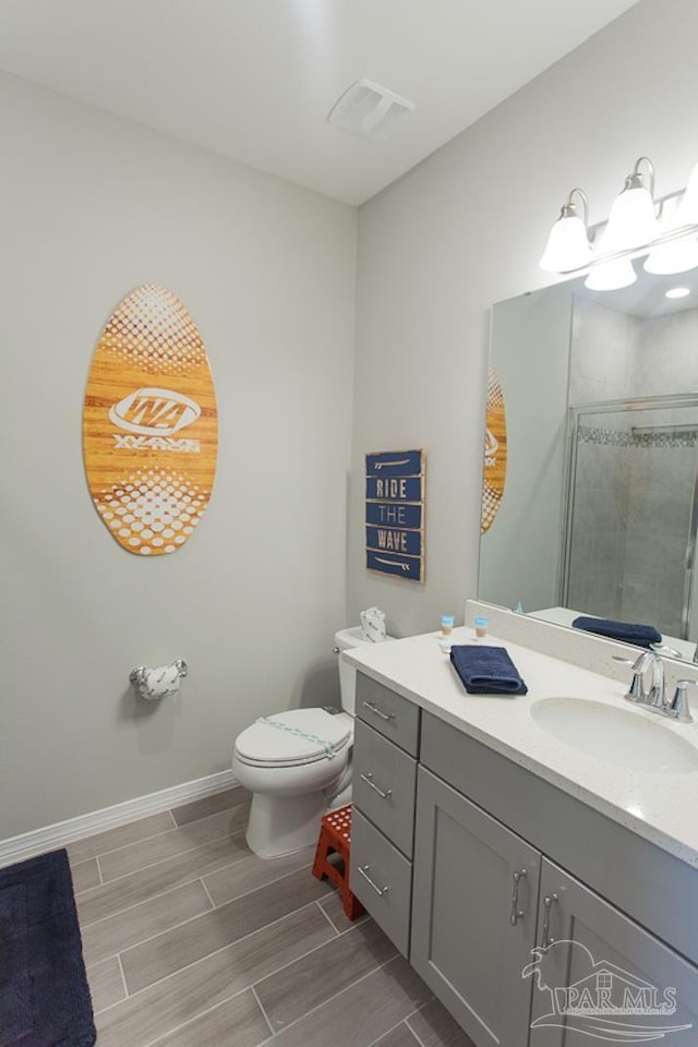 bathroom featuring toilet, vanity, baseboards, wood finish floors, and a stall shower