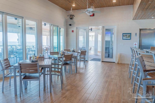 dining room with light wood-type flooring, wooden ceiling, ceiling fan, and a towering ceiling