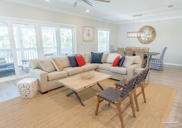 living room featuring light wood-type flooring, baseboards, visible vents, ceiling fan with notable chandelier, and ornamental molding