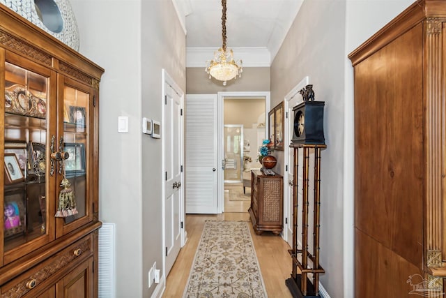 hall with ornamental molding, light wood-type flooring, and an inviting chandelier