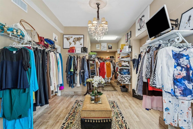 spacious closet with light hardwood / wood-style flooring and an inviting chandelier