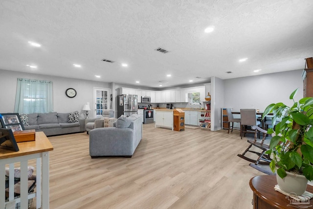 living area featuring light wood-type flooring, visible vents, a textured ceiling, and recessed lighting