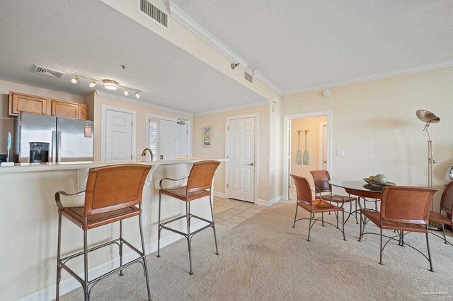 kitchen with a kitchen bar, track lighting, stainless steel fridge, crown molding, and light colored carpet