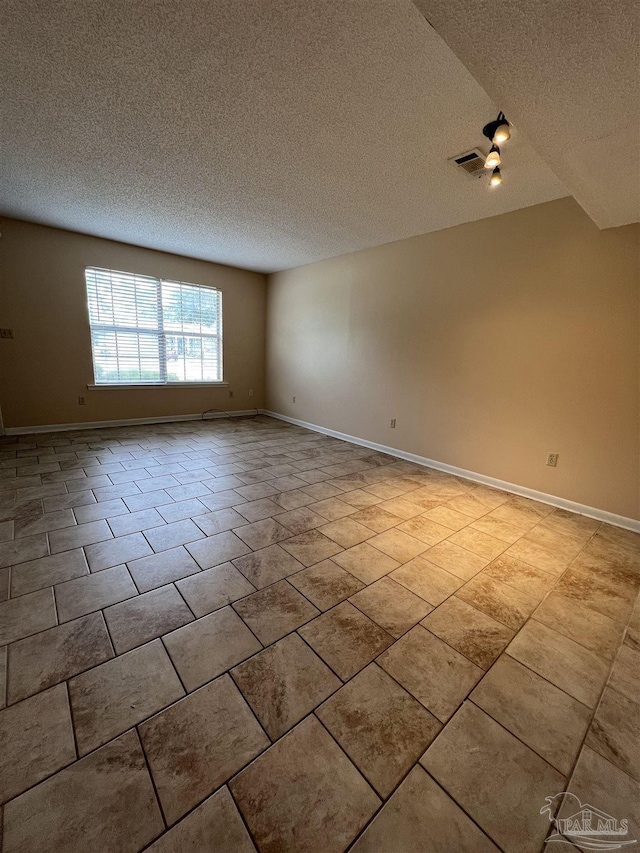 empty room featuring a textured ceiling, light tile patterned flooring, visible vents, and baseboards