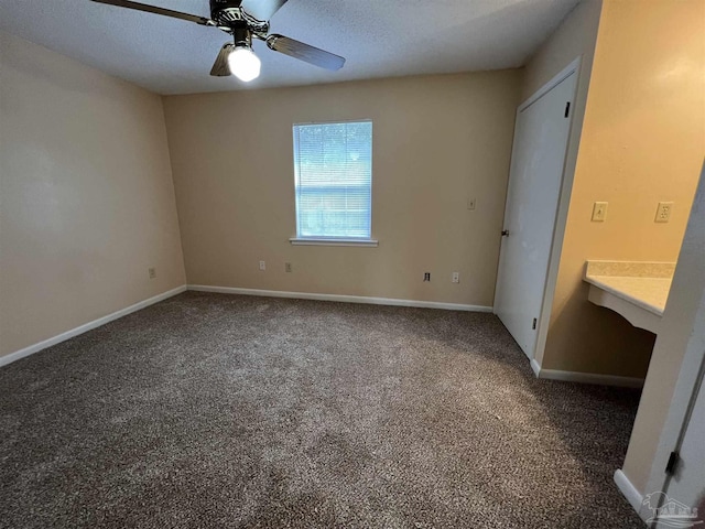 unfurnished bedroom with ceiling fan, a textured ceiling, dark carpet, and baseboards