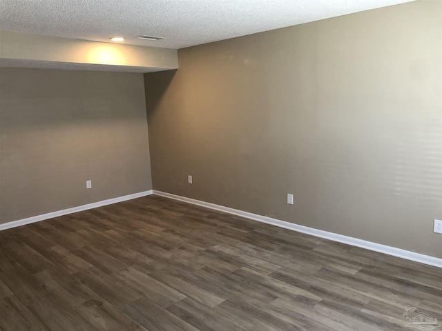 empty room with dark wood finished floors, a textured ceiling, and baseboards