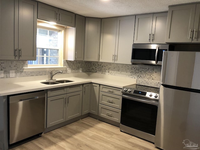 kitchen with stainless steel appliances, light countertops, gray cabinetry, light wood-type flooring, and a sink