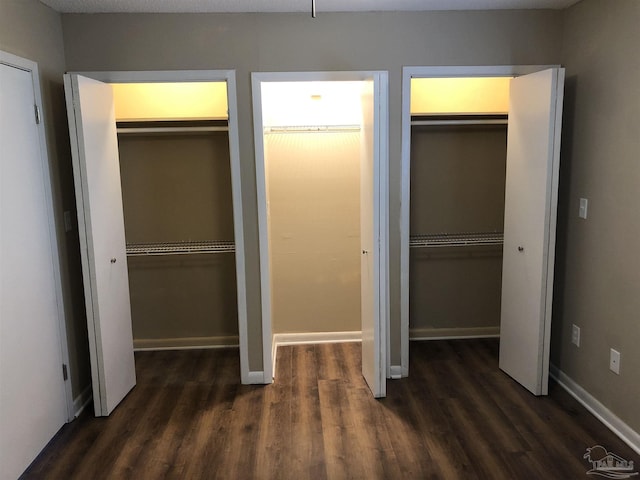 unfurnished bedroom with dark wood-style flooring, baseboards, and two closets