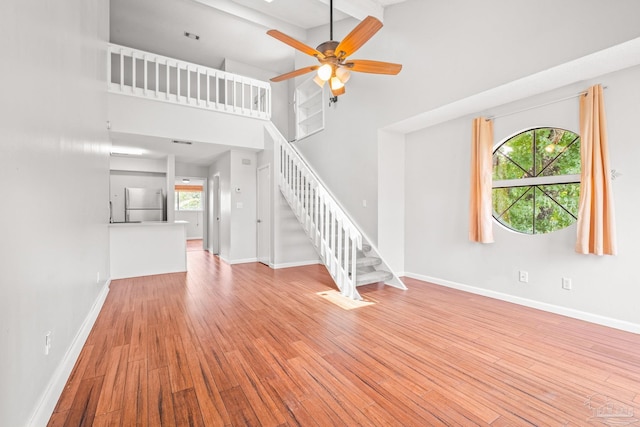 unfurnished living room featuring ceiling fan, light hardwood / wood-style floors, a wealth of natural light, and a high ceiling