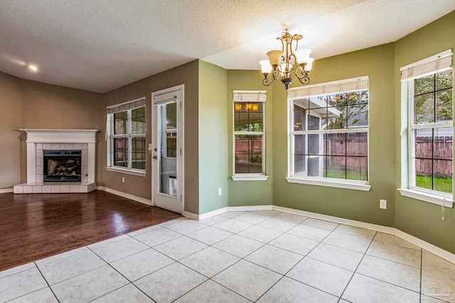 unfurnished dining area featuring a fireplace, light hardwood / wood-style flooring, a textured ceiling, and a notable chandelier