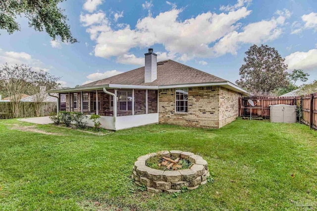 back of property featuring a sunroom, a yard, a patio, and a fire pit