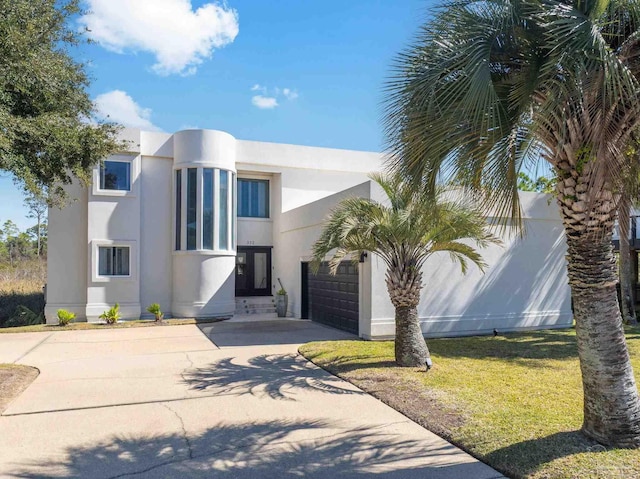 art deco home with concrete driveway, a garage, a front yard, and stucco siding