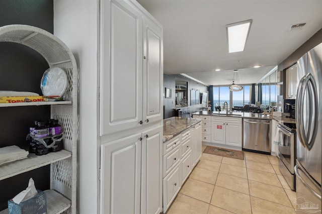 kitchen featuring a sink, white cabinetry, a peninsula, appliances with stainless steel finishes, and light tile patterned floors