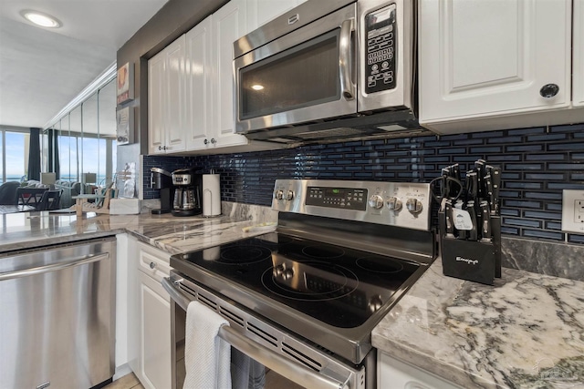 kitchen with stainless steel appliances, light stone countertops, tasteful backsplash, and white cabinetry