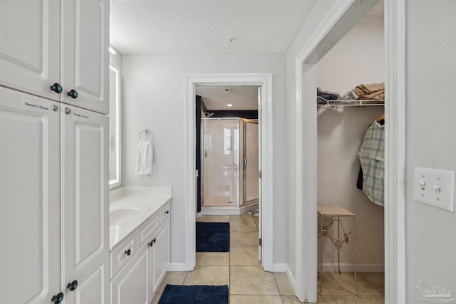 full bathroom featuring tile patterned floors, a stall shower, a textured ceiling, vanity, and a spacious closet