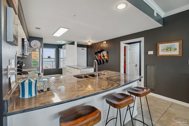 kitchen with a sink, visible vents, light tile patterned flooring, and white cabinetry