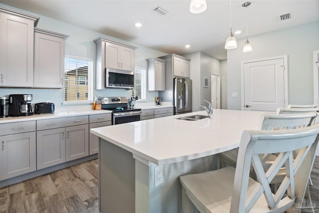 kitchen featuring hardwood / wood-style floors, pendant lighting, a kitchen breakfast bar, sink, and appliances with stainless steel finishes