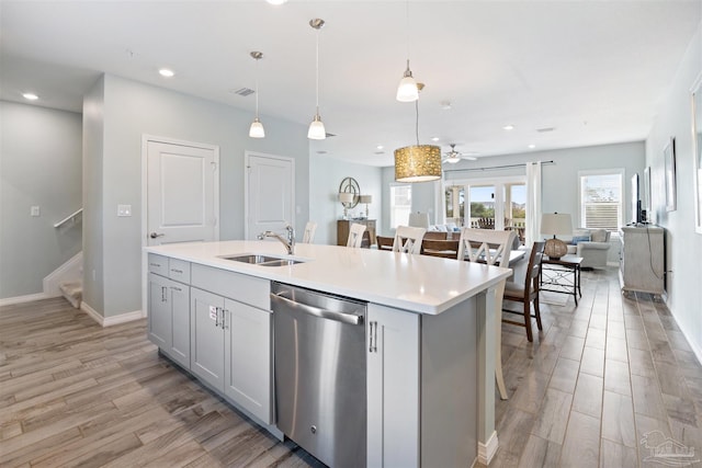 kitchen featuring pendant lighting, dishwasher, light wood-type flooring, and a kitchen island with sink