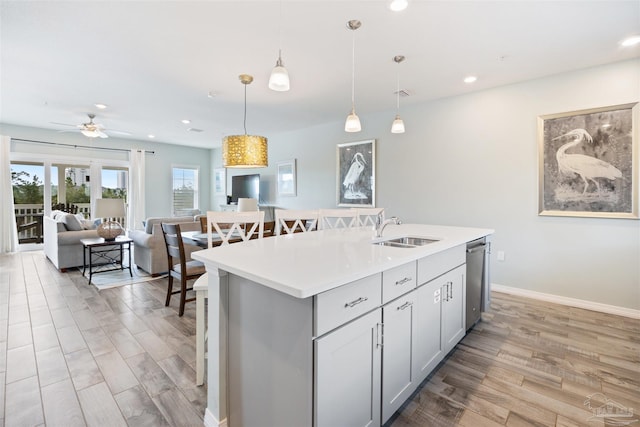 kitchen featuring pendant lighting, dishwasher, a kitchen island with sink, gray cabinets, and light wood-type flooring