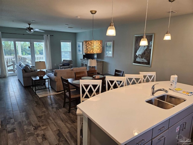 kitchen featuring ceiling fan, dark wood-type flooring, sink, decorative light fixtures, and a center island with sink