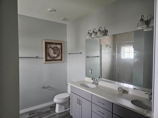 bathroom with vanity, toilet, a textured ceiling, a tile shower, and wood-type flooring