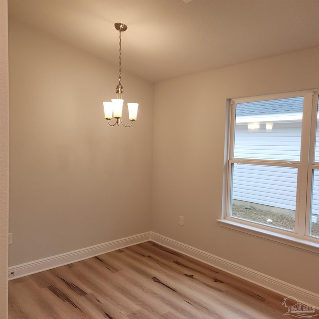 spare room featuring lofted ceiling, a healthy amount of sunlight, wood-type flooring, and a chandelier