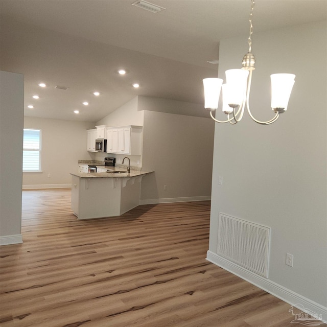 kitchen featuring a breakfast bar, kitchen peninsula, hanging light fixtures, appliances with stainless steel finishes, and white cabinetry