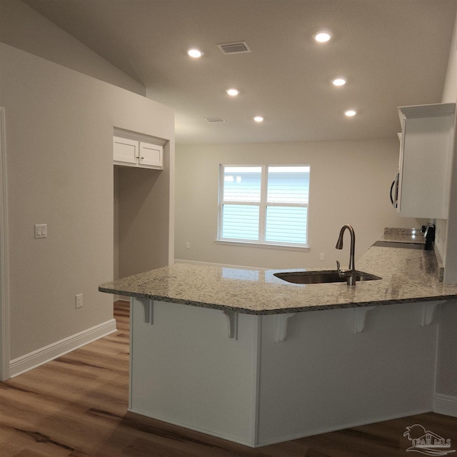 kitchen with white cabinets, sink, light stone countertops, a kitchen bar, and kitchen peninsula