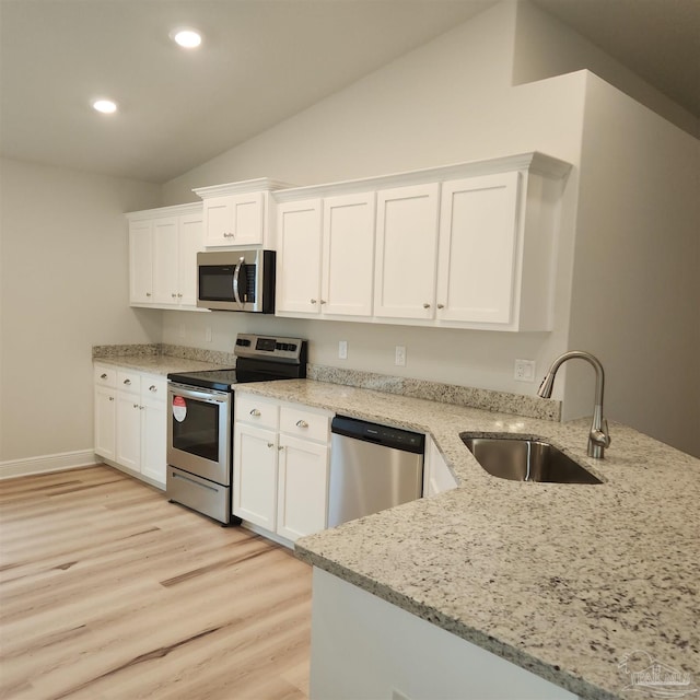 kitchen with sink, light stone countertops, appliances with stainless steel finishes, white cabinetry, and kitchen peninsula