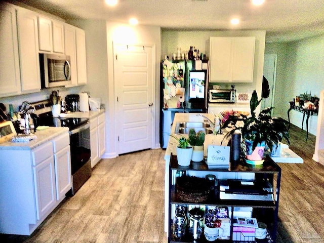 kitchen with light hardwood / wood-style floors, black appliances, a textured ceiling, and white cabinetry