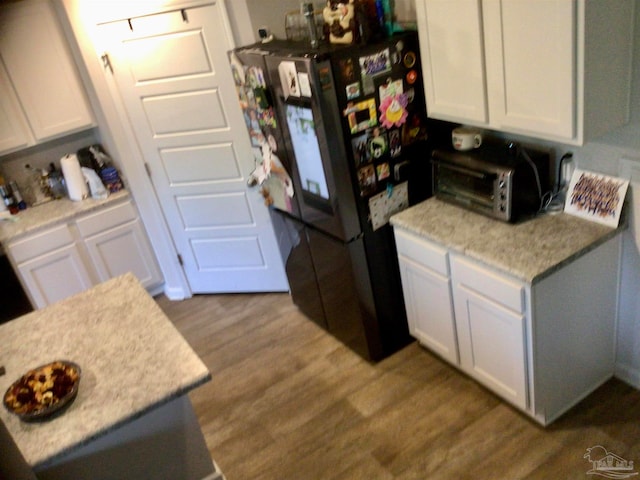 kitchen featuring black refrigerator, light hardwood / wood-style floors, and white cabinetry