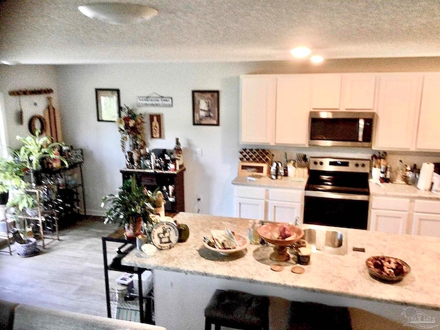 kitchen featuring a textured ceiling, white cabinetry, stainless steel appliances, a kitchen breakfast bar, and light hardwood / wood-style floors