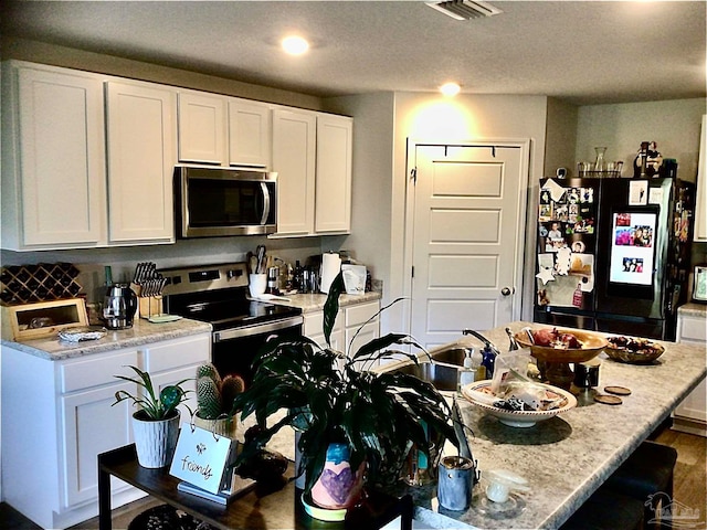 kitchen featuring an island with sink, appliances with stainless steel finishes, light stone counters, and white cabinetry