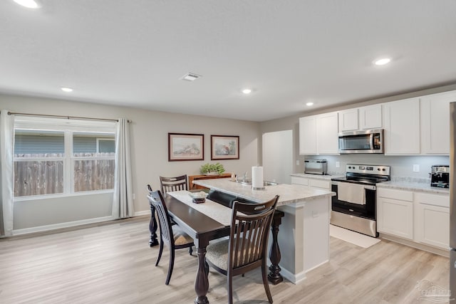 kitchen with appliances with stainless steel finishes, light wood finished floors, a center island with sink, and light countertops