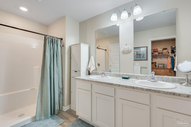 bathroom featuring wood finished floors, a sink, a shower stall, and double vanity