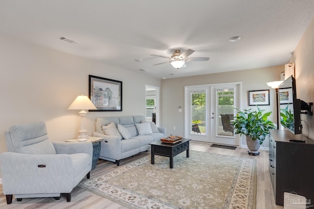 living room featuring visible vents, light wood finished floors, and a ceiling fan