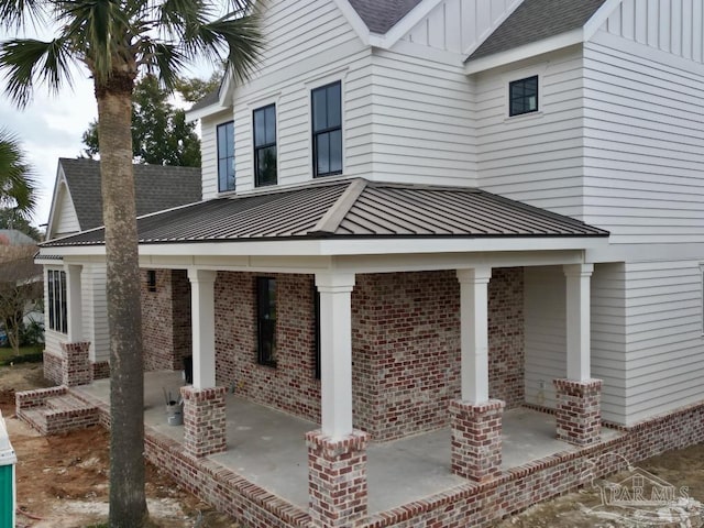 view of property exterior featuring a standing seam roof, board and batten siding, a shingled roof, metal roof, and brick siding