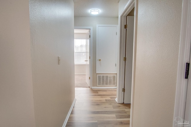 corridor with a textured ceiling and light wood-type flooring