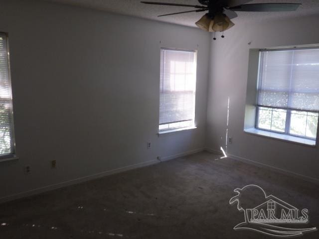 spare room featuring dark colored carpet, plenty of natural light, and ceiling fan