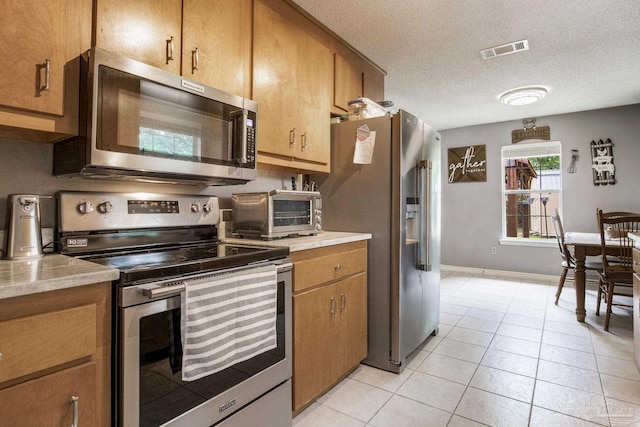 2661 Avenida De Sol, Navarre, FL 32566 - kitchen with stainless steel appliances, light countertops, light tile patterned flooring, brown cabinetry, and a textured ceiling