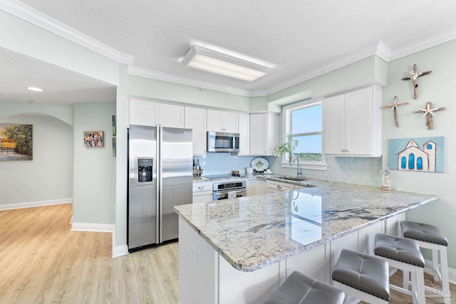 kitchen featuring a peninsula, appliances with stainless steel finishes, white cabinetry, and a kitchen breakfast bar