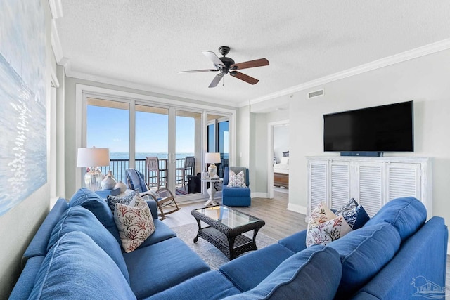 living area featuring a textured ceiling, visible vents, baseboards, ornamental molding, and light wood-type flooring