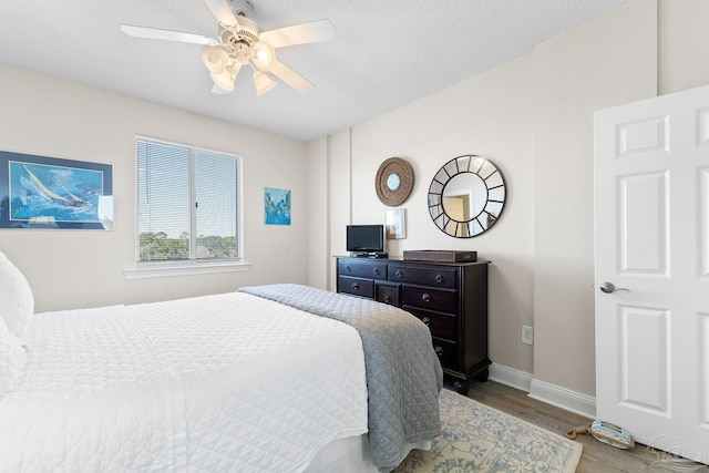 bedroom featuring ceiling fan, a textured ceiling, baseboards, and wood finished floors